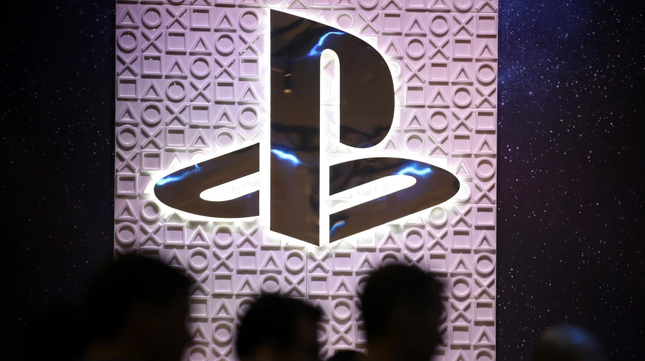 The PlayStation logo hangs over people's heads as they walk by. 